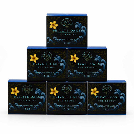 Six rectangular bars of Private Oaks The Resort Handcrafted Bar Soap arranged in a pyramid stack on a white background. Each dark blue soap box features a yellow flower graphic and white text.