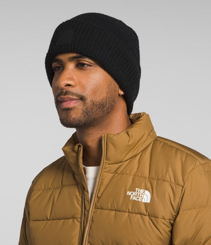 Man wearing a black beanie and brown The North Face jacket on a gray background