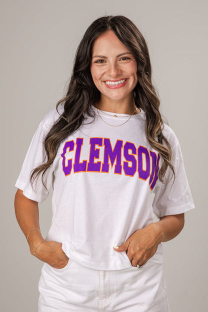 Woman wearing a white t-shirt with 'Clemson' printed in purple and yellow.